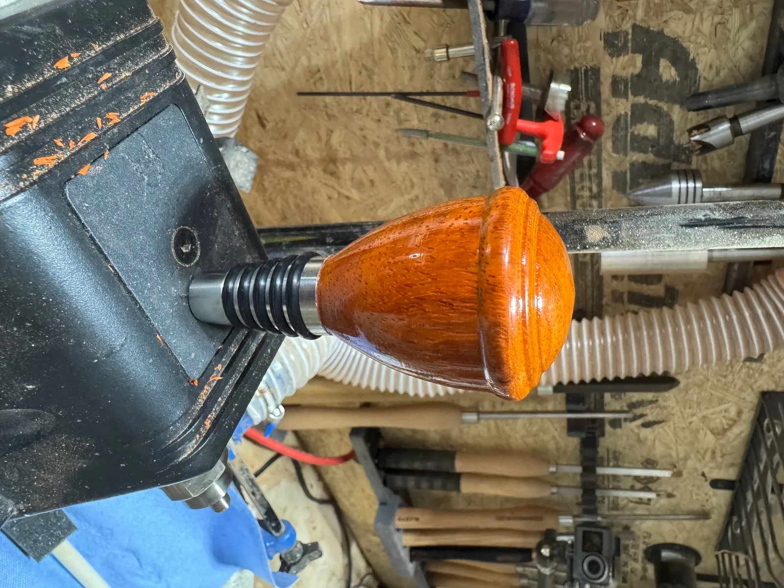 A padauk bottle stopper being turned on the lathe, showing the warm orange color of the wood